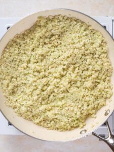 A skillet filled with cooked riced cauliflower sits on a stovetop.