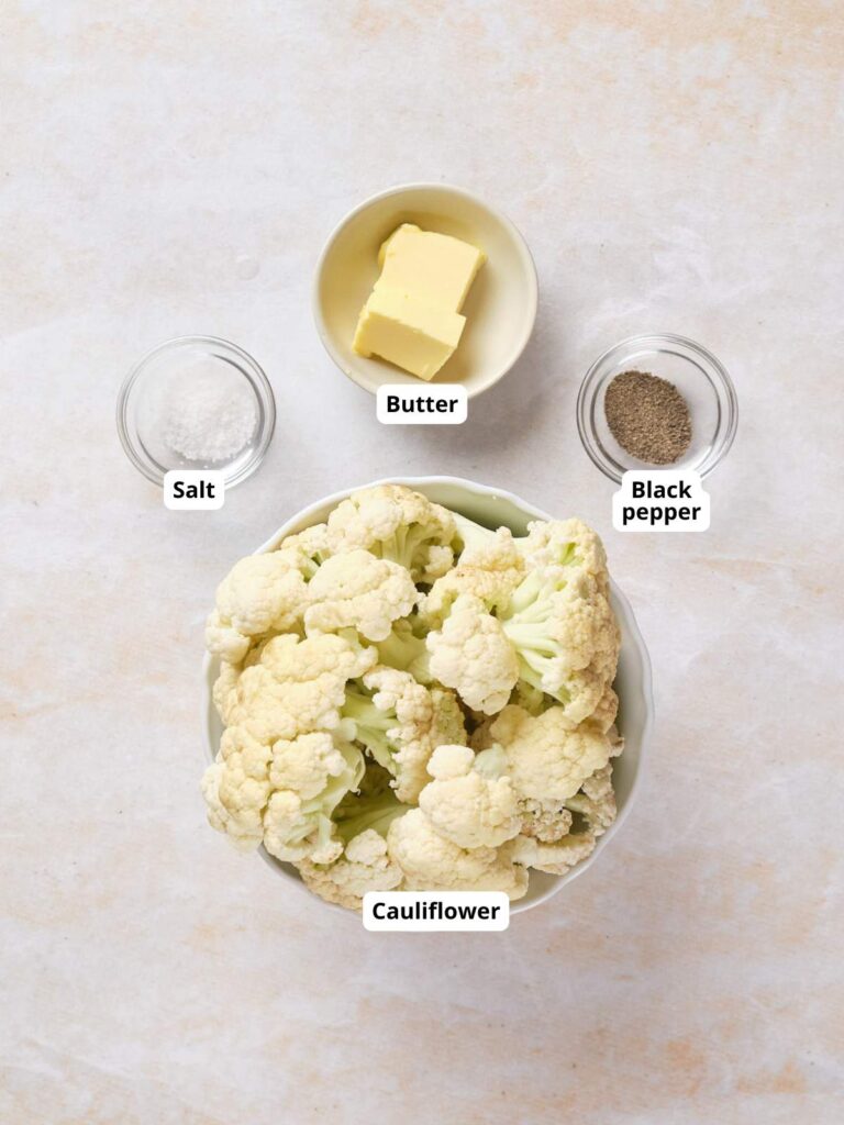 A bowl of cauliflower florets, a dish of butter, a dish of salt, and a dish of black pepper arranged on a light surface, each labeled.