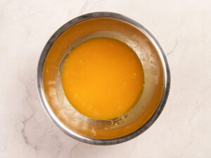 A stainless steel bowl containing a smooth, yellow-orange liquid mixture on a light-colored countertop.