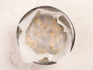 A metal bowl contains dough covered with parchment paper, resting on a light-colored countertop.