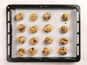 Sixteen unbaked chocolate chip cookie dough balls arranged on a parchment-lined baking sheet, ready to go into the oven.