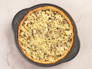 A round pie tin filled with a baked pie featuring a golden crust and a topping of grated cheese and cooked ground meat.