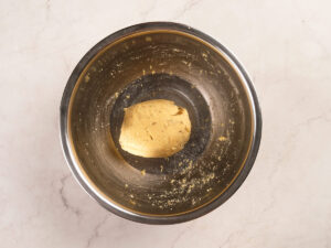 A ball of cookie dough sits in the center of a stainless steel mixing bowl on a light marble countertop.
