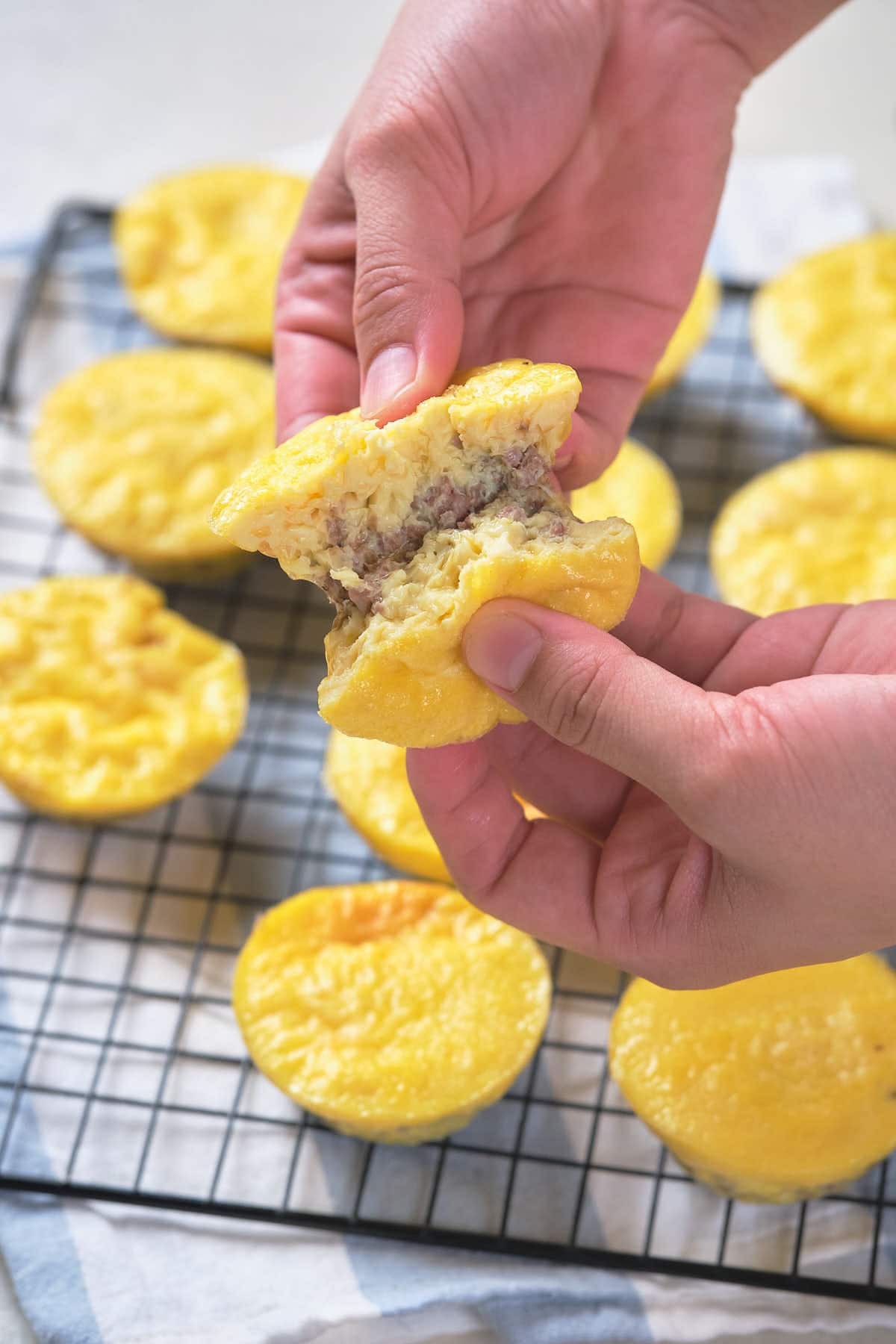 A person holds a half-eaten yellow pastry with meat filling above a cooling rack with several whole pastries.