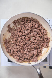 Cooked ground beef in a large skillet on a stovetop, shown from above.