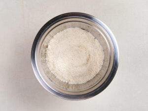 A metal bowl filled with finely ground, light-colored flour sits on a light-colored surface.