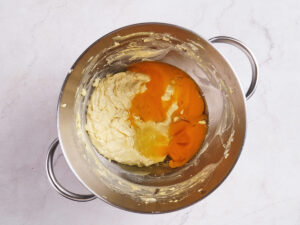 A mixing bowl containing creamed butter and sugar on one side and raw eggs on the other, ready to be combined.