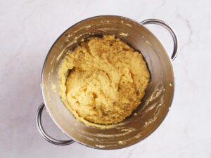 A metal mixing bowl filled with yellow, thick cornbread batter sits on a light-colored countertop.
