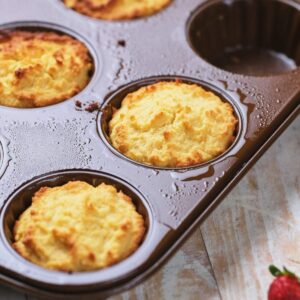 A close-up of freshly baked muffins in a non-stick muffin tray, with some cups empty and the tray resting on a wooden surface.