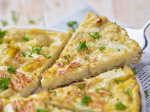 A close-up of a sliced cauliflower frittata garnished with chopped parsley on a white plate.