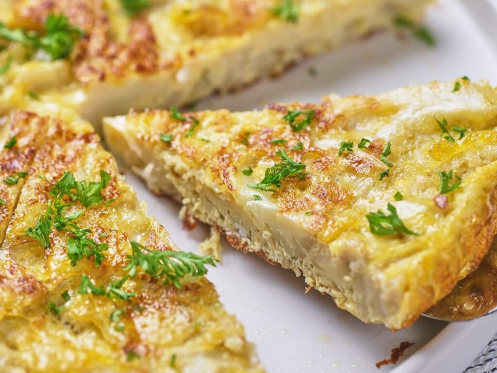 Close-up of sliced Spanish omelette on a white plate, garnished with chopped parsley.