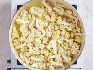 A pot filled with chopped cauliflower florets sits on a stovetop, viewed from above.