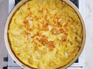 A large skillet filled with a baked yellow casserole, possibly cheesy or egg-based, sits on a stovetop.