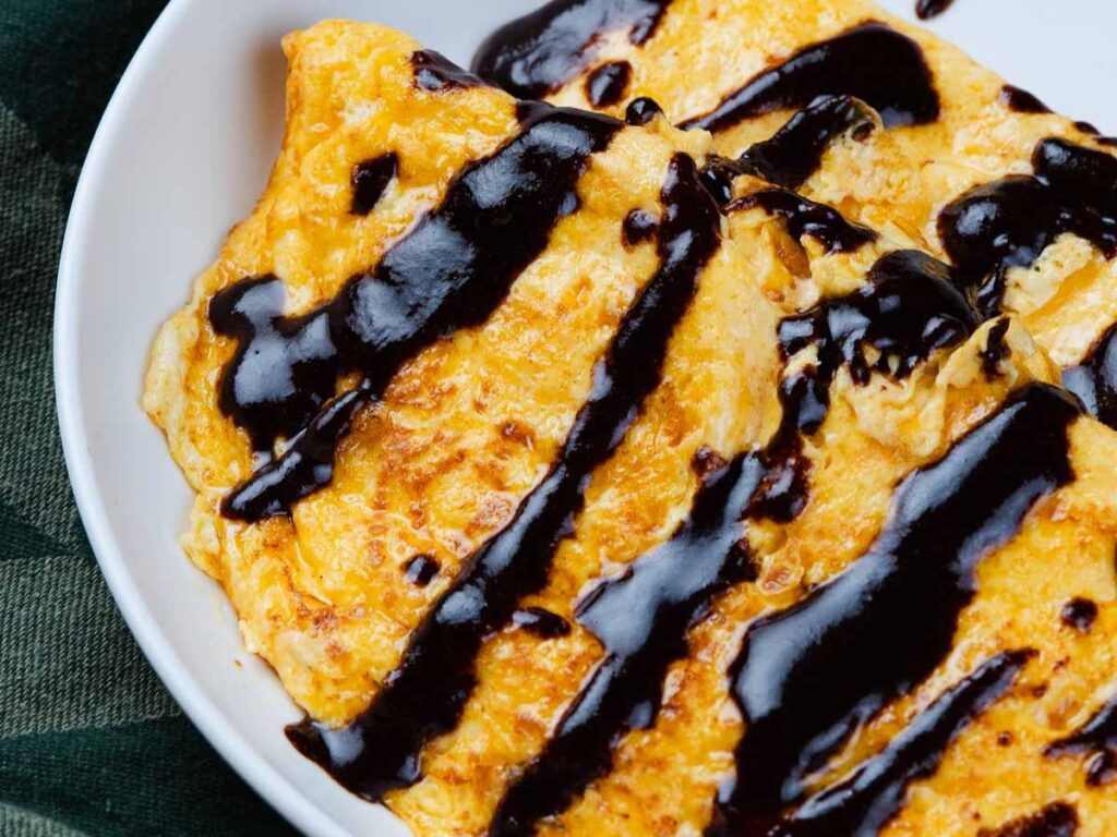 An omelet drizzled with dark sauce in a white bowl.