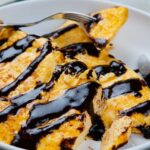 A plate of cooked egg topped with dark chocolate sauce, being eaten with a fork.