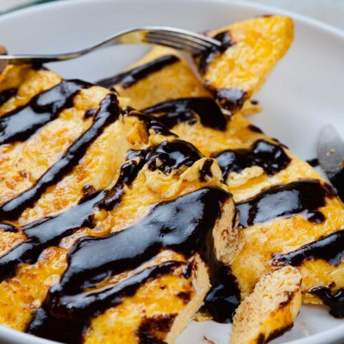 A plate of cooked egg topped with dark chocolate sauce, being eaten with a fork.