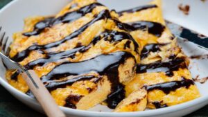 A cooked omelet drizzled with chocolate sauce in a white bowl with a fork.