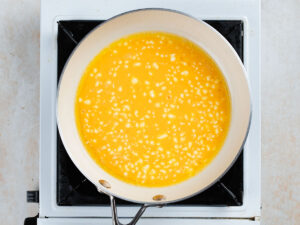 Eggs beginning to scramble in a frying pan on a stovetop.