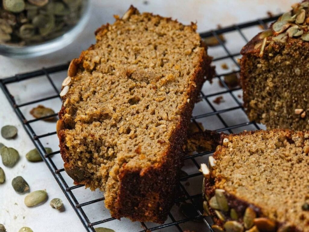 Slices of pumpkin bread topped with pepitas resting on a wire cooling rack.