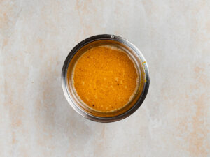 A metal bowl containing an orange, whisked liquid mixture.