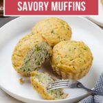 Three keto savory breakfast muffins with broccoli on a white plate, one broken open with a fork.