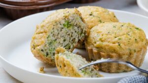 Three broccoli muffins on a white plate, with one broken open to show the interior.
