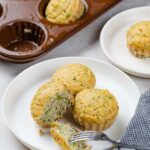Savory broccoli muffins in a muffin tin and on white plates, with one broken open by a fork.