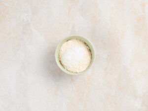 A small green bowl containing a mound of beige granular powder topped with a scoop of white powder.